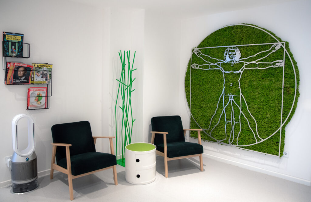 Wartebereich der Praxis mit zwei Sesseln und einem vitruvianischen Menschen aus Moos an der Wand